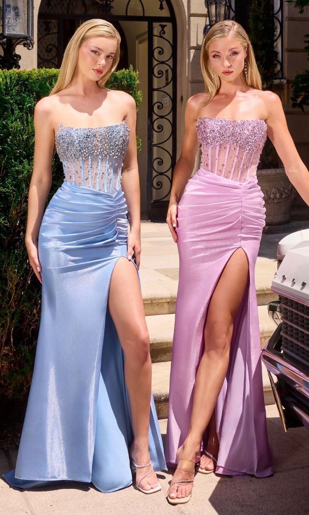 Two women stand outdoors in Ladivine CW301 gowns—strapless prom dresses with sheer, beaded corset bodices and split-thigh skirts; one is light blue, the other light pink.